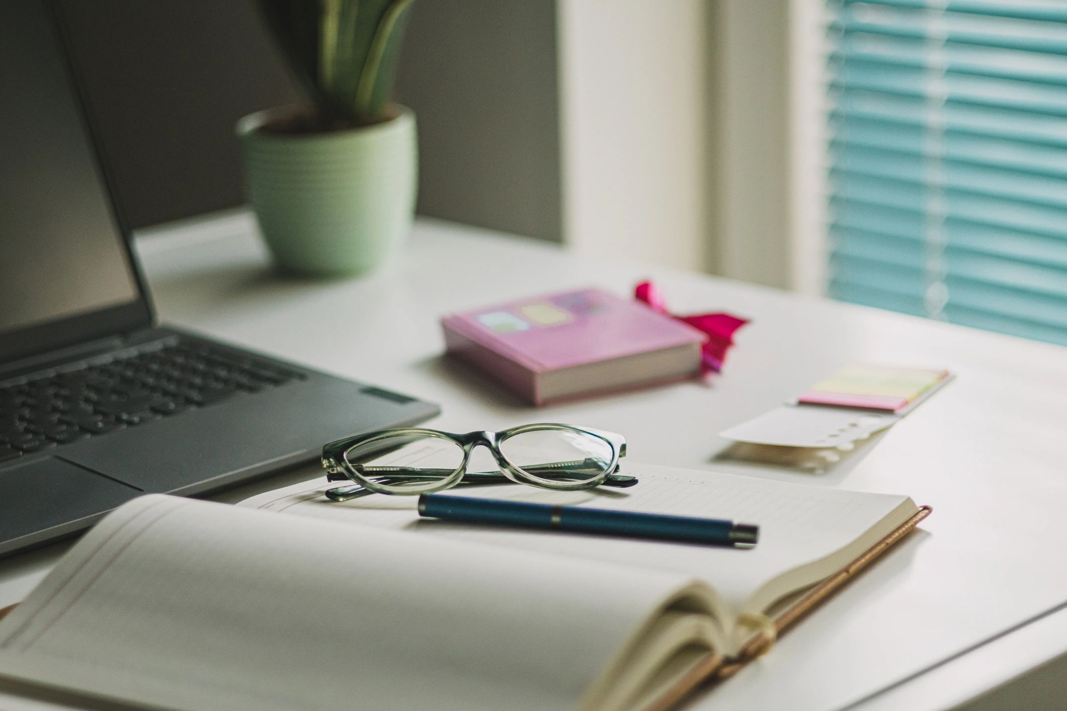 Women's office desk table. Laptop computer, cup of coffee, reading glasses and office supplies.