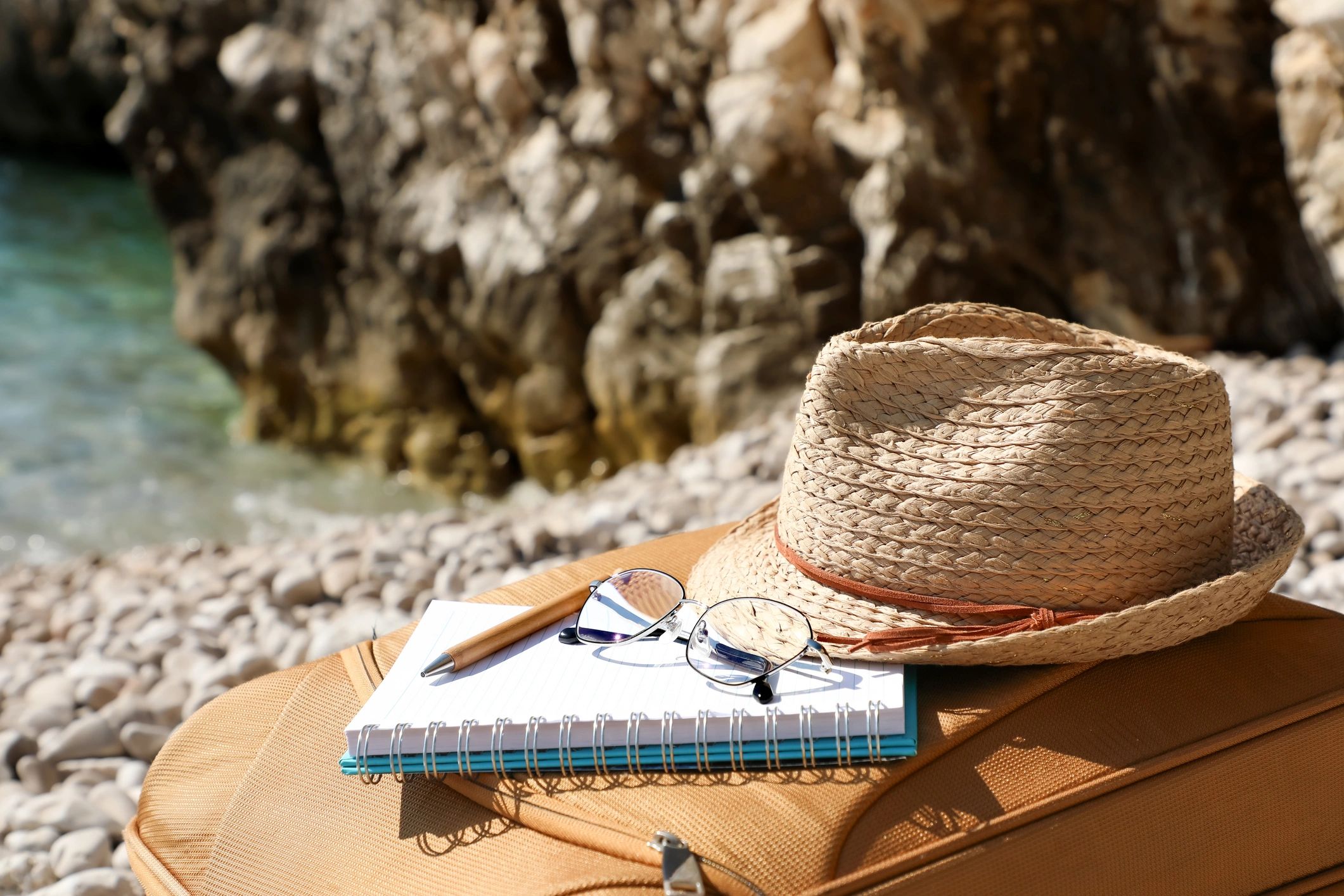 Suitcase by the sea with notebook and straw hat